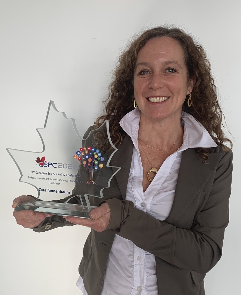 A picture of a woman with curly hair holding a leaf-shaped glass trophy