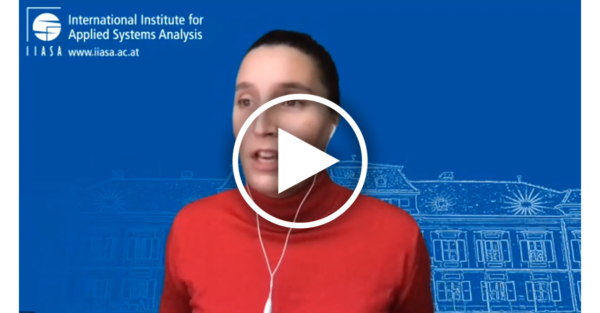a white woman in a red shirt over a blue background with a play button overlaid