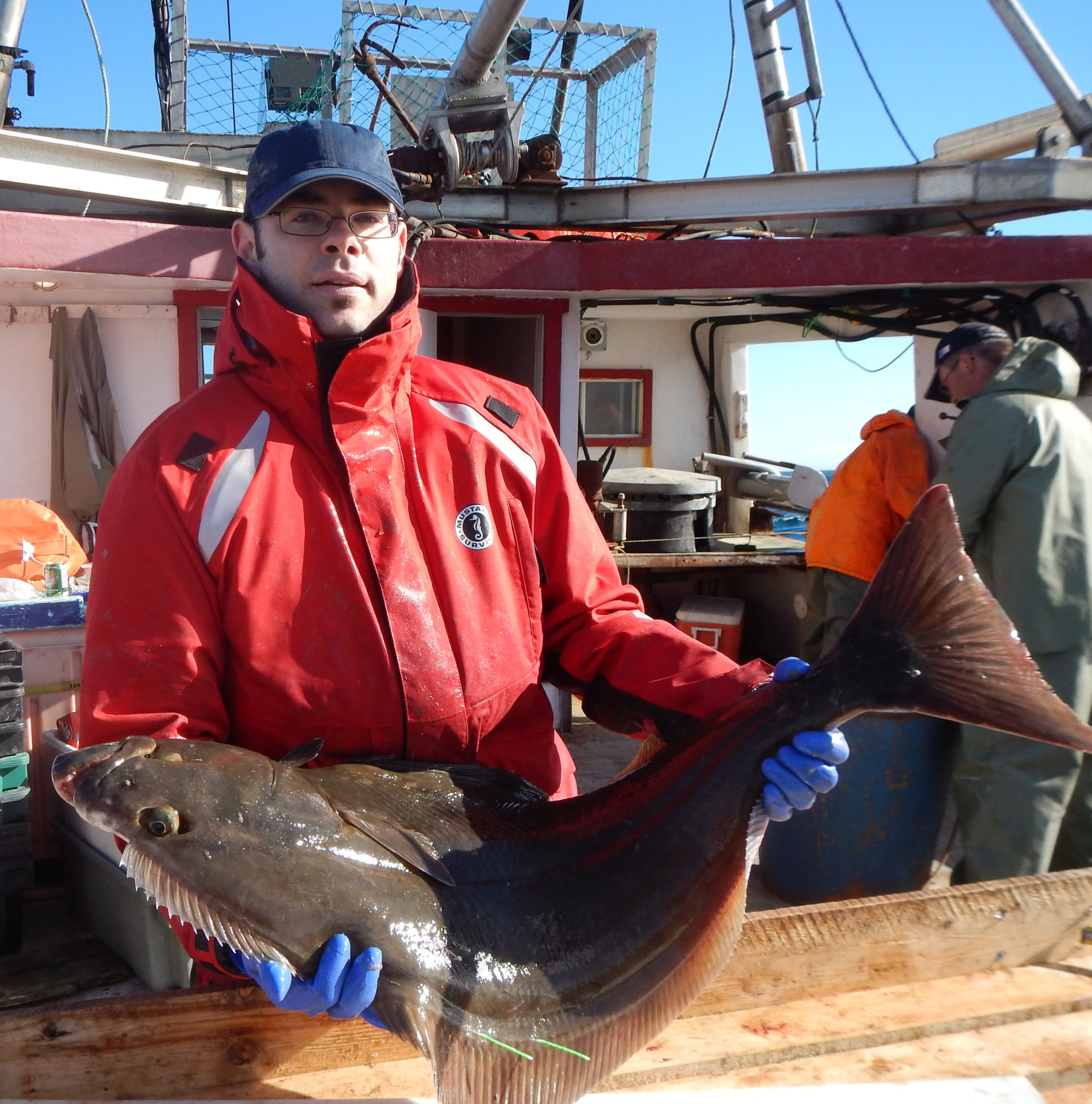 Photo of a white man holding a fish on a fishing vessel