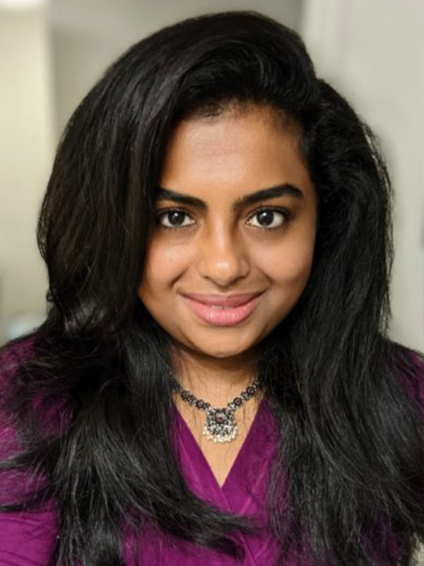 A headshot of an indian woman with long hair and a purple shirt