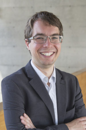 A headshot of a white man in a suit and glasses.