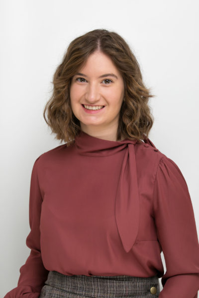 Un portrait d'une femme blanche aux cheveux bruns courts et un chemisier rouge.