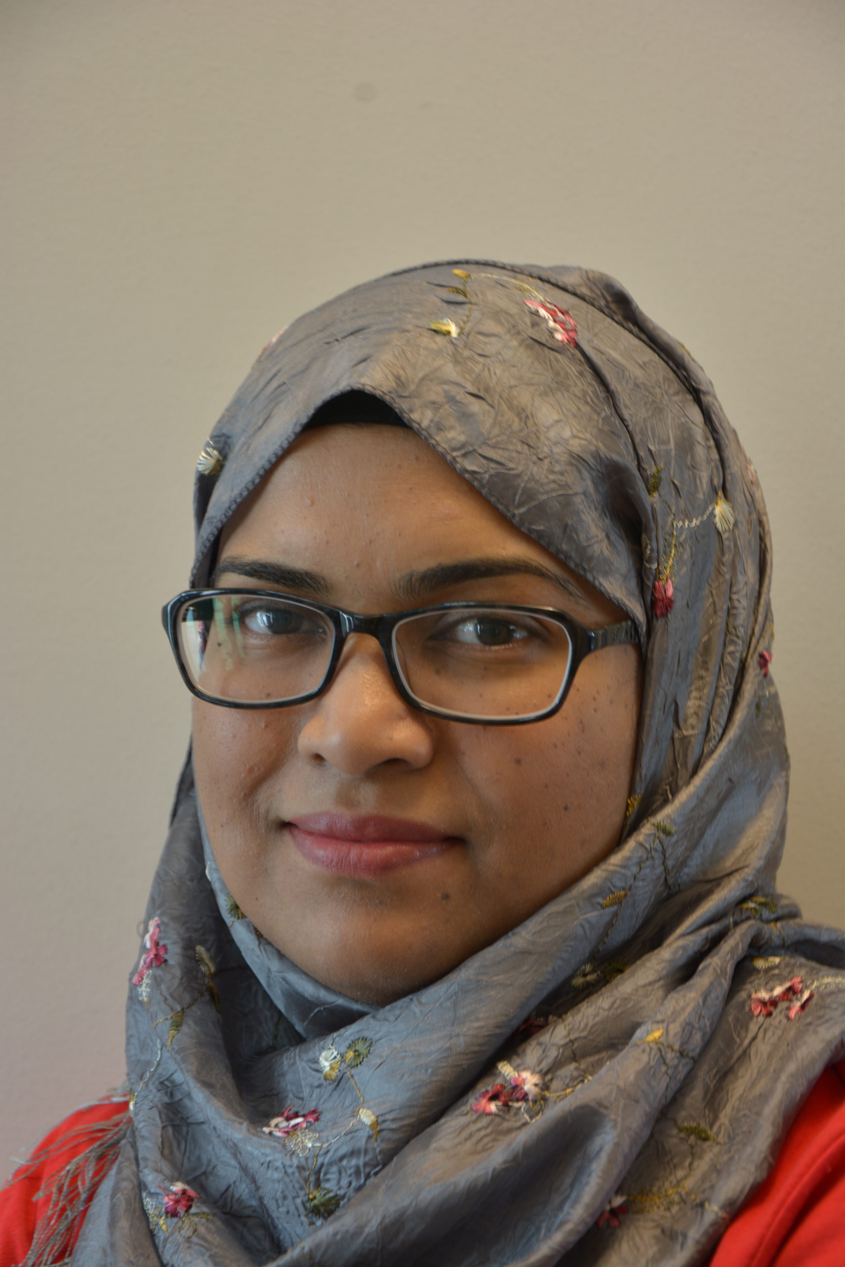 Headshot of a brown skin woman in glasses and a grey hijab.