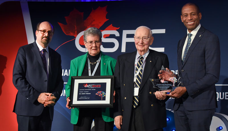 Dr. Henry Friesen holding award with three award presenters